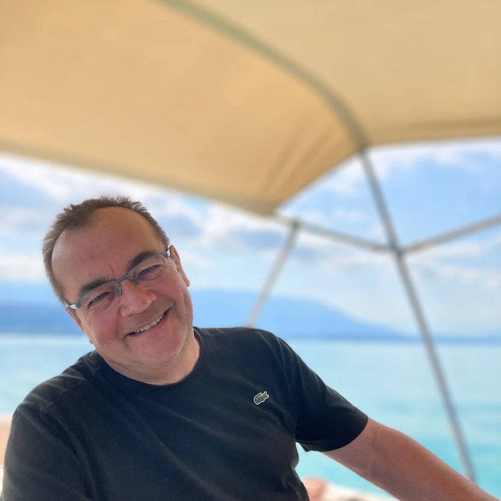 Philippe sur un bateau avec un paysage de lac avec montagnes en arrière plan.