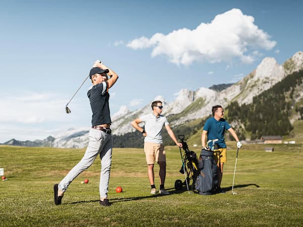 Golfeurs en action au golf des Confins, avec vue sur les montagnes de La Clusaz et des Aravis.