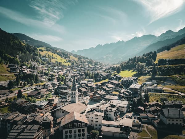 Vue aérienne du village de la Clusaz avec le village au premier plan et les montagnes des Aravis en arrière plan.