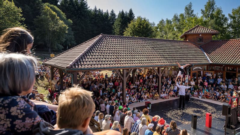 Spectacle en plein air au Col de Crie devant un large public, dans un cadre naturel boisé devant le bâtiment de la maison de la randonnée et du trail.