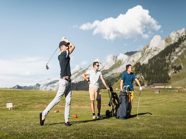 Golfeurs en action au golf des Confins, avec vue sur les montagnes de La Clusaz et des Aravis.