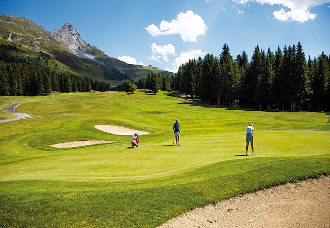 Golf de Méribel avec joueurs sur le parcours entouré de montagnes et de forêts.