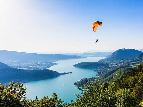 Vue aérienne du lac d'Annecy avec les montagnes et un parapente.